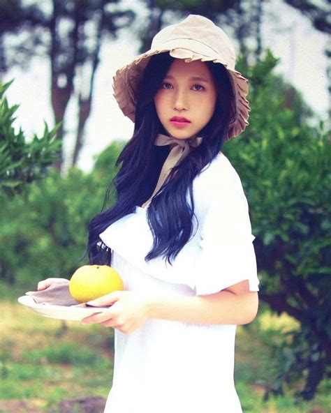 a woman in a hat holding an orange and a lemon on a white plate with trees in the background