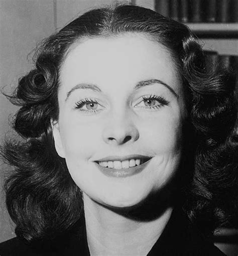 a black and white photo of a woman with curly hair smiling at the camera, in front of bookshelves