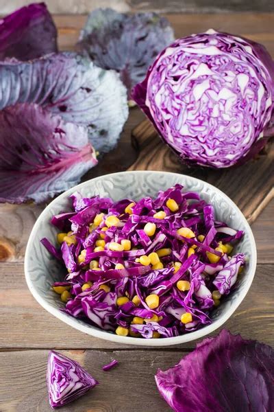 Red cabbage salad with corn grains in a plate on a wooden table. Vegetarian food. Close-up ...