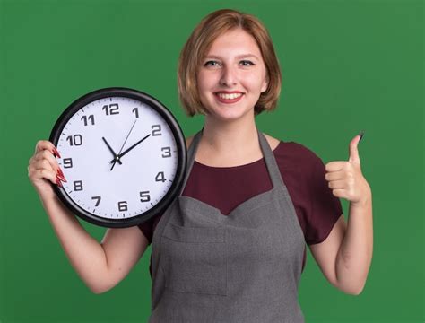 Free Photo | Young beautiful woman hairdresser in apron holding wall clock looking at front with ...