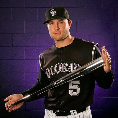 a man holding a baseball bat in front of a purple brick wall with the ...