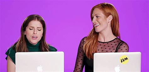 two women are laughing while looking at their laptops