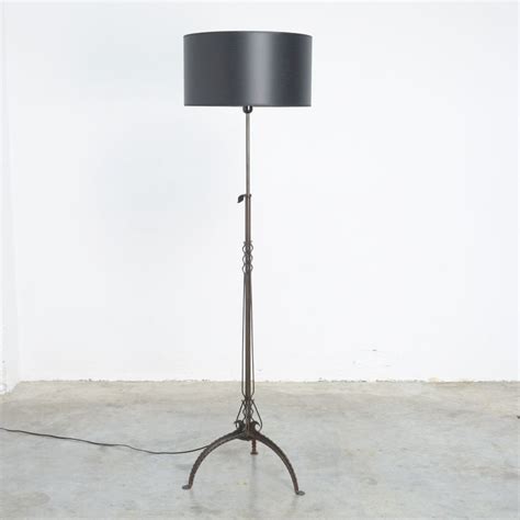 a floor lamp with a black shade on the top and an iron base, in front of a white wall