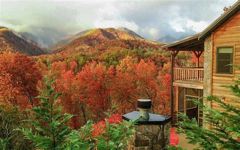 a cabin in the mountains surrounded by trees with autumn foliage on it's sides