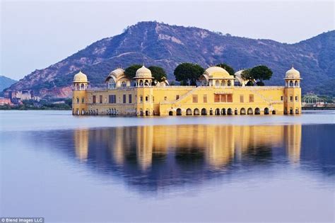 a white swan flying over a lake next to a large yellow building with ...