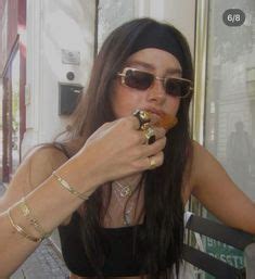 a woman wearing sunglasses and eating food in front of a store window with her hands on her hips