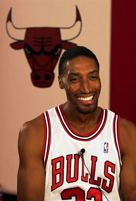 a basketball player smiles while standing in front of a bulls logo on the wall behind him