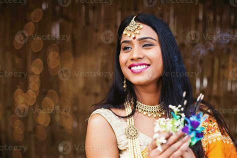 Beautiful Indian woman in traditional clothes and jewelry praying and offering flowers and ...