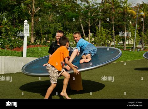 Three young barefoot boys laughing spinning on big rotating disk at ...