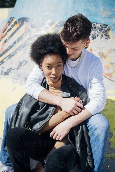 Boyfriend hugging girlfriend while sitting at skateboard park stock photo