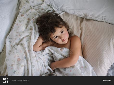 Little girl lying in a bed wrapped in sheets stock photo - OFFSET