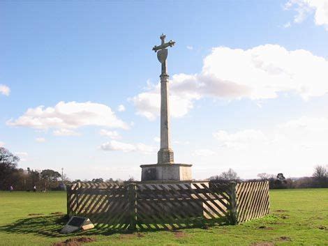 a statue in the middle of a field with a cross at the top and a book on the ground next to it