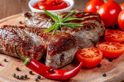 Delicious steaks with rosemary, tomatoes, chili and sauce on wooden kitchen Board - Creative ...