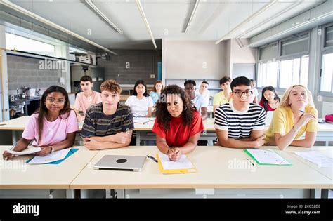 Confident group of university college sitting at classroom looking at camera with serious face ...