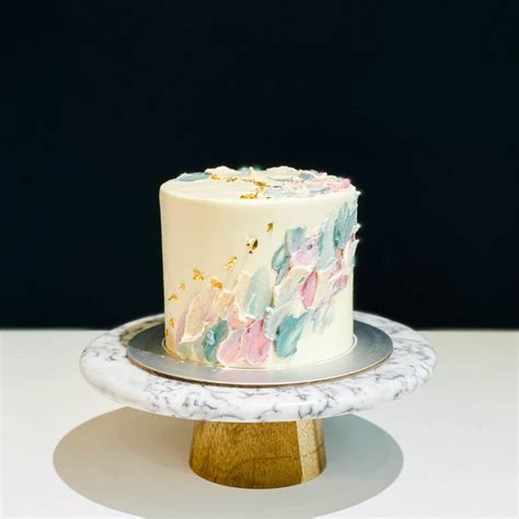 a white and blue cake sitting on top of a wooden stand next to a black wall