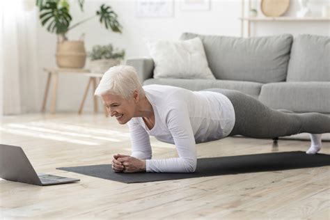 Sporty senior woman doing yoga plank while watching tutorial on laptop ...