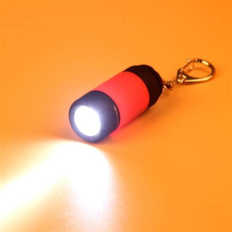 a red and black flashlight keychain on an orange surface with light coming from it