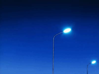 two street lamps on the side of an empty road at night with blue sky in background