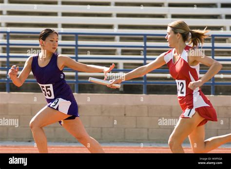 Female track athlete passing relay baton to another one Stock Photo - Alamy