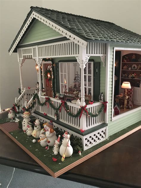 a doll house with snowmen and christmas decorations on the front porch, including lights