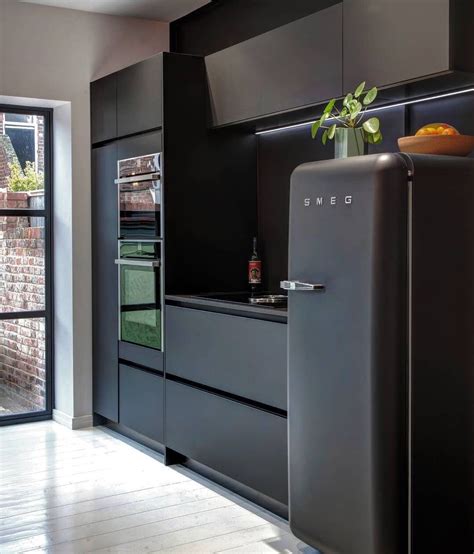 a black refrigerator freezer sitting inside of a kitchen next to a brick wall and door