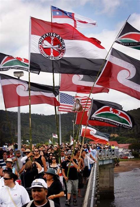 A large number of Māori flags are being flown as a large group crosses the bridge at Waitangi ...