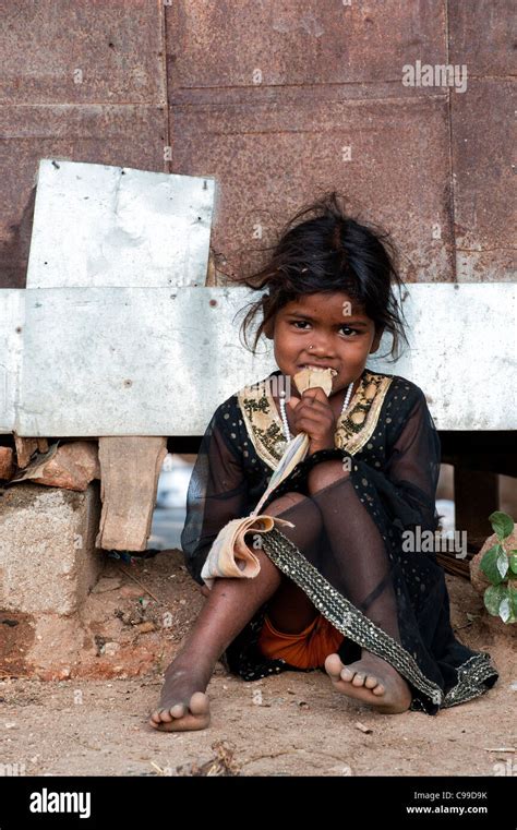 Poor Indian nomadic beggar girl sitting against a hut eating a biscuit. Andhra Pradesh, India ...