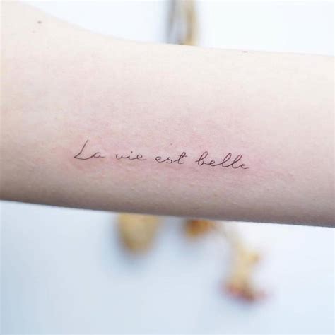 "La vie est belle" lettering tattoo on the inner arm.