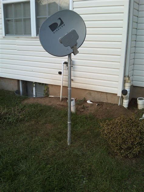 a satellite dish sitting on top of a metal pole in front of a white house