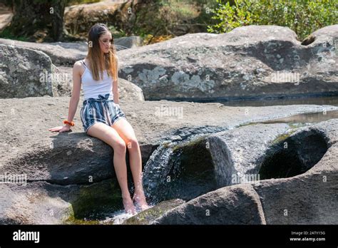 Attractive teenage girl sitting on rock ledge with legs splashing cool ...