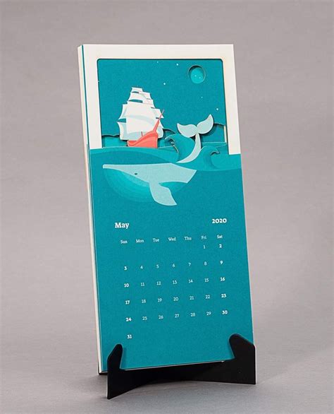 a desk calendar with an image of a boat and whale on the water, in front of a gray background