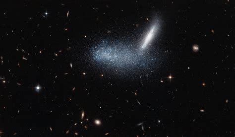 In the foreground, the irregular dwarf galaxy PGC 16389 — seen here as ...