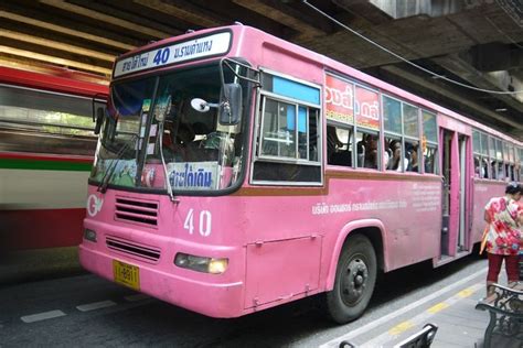 a pink bus is parked in front of a train station as people board the bus