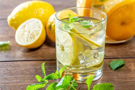 A glass of lemonade with ice cubes, sliced citrus and mint on old ...