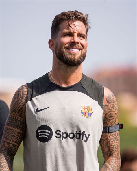 a man with tattoos on his arms and chest smiles while standing in front ...