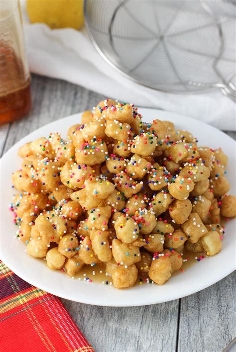 Struffoli are fried dough balls that are covered in honey and sprinkles, all served in a mound ...