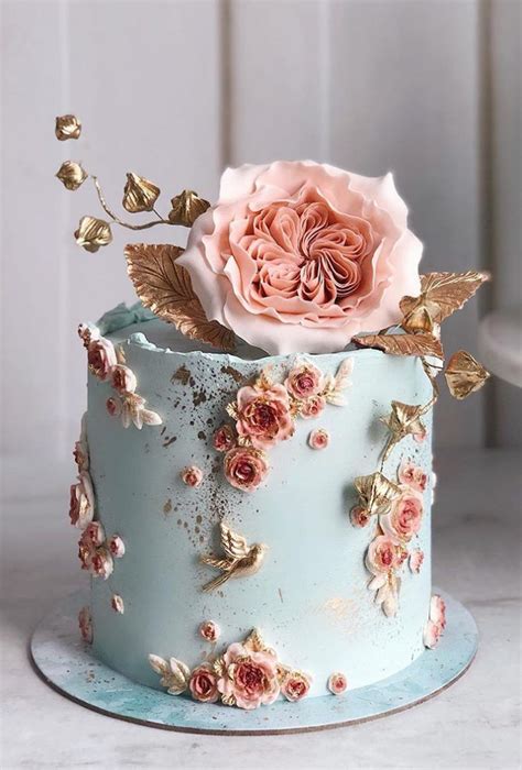 a blue cake with pink flowers on top and gold leaves around the edges ...