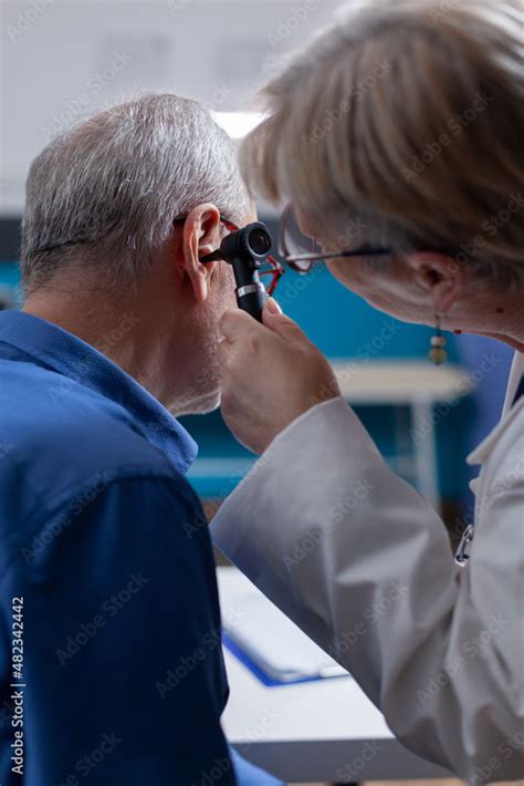 Close up of medic using otoscope to do ear examination for aged patient in cabinet. General ...