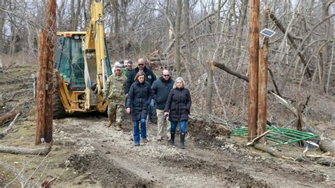 several people walking on a dirt path in the woods with a bulldozer behind them