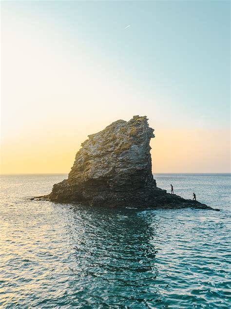 Two people standing on rock formation surrounded by body of water ...