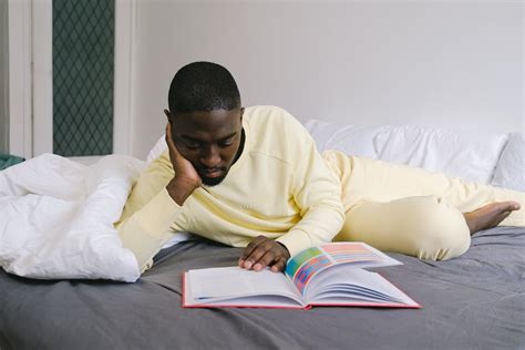 Man in Yellow Sweater Reading a Book on Bed · Free Stock Photo