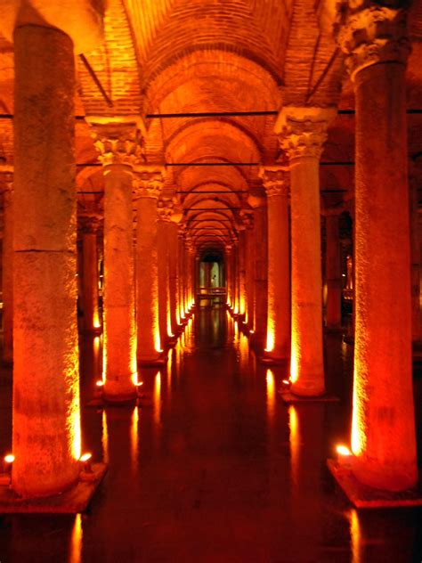 the inside of an old building with columns and lights on it's sides, all lit up at night