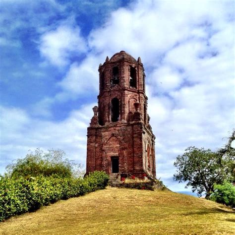 a very tall tower sitting on top of a lush green hillside under a cloudy blue sky