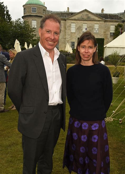 a man and woman standing in front of a building with people around them on the grass