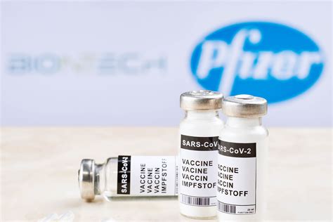 Covid-19 vaccine and syringe against Biontech and Pfizer logos ...