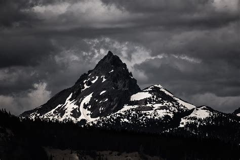 A desaturated shot of a dark mountain covered in patches of white snow under a gray sky ...