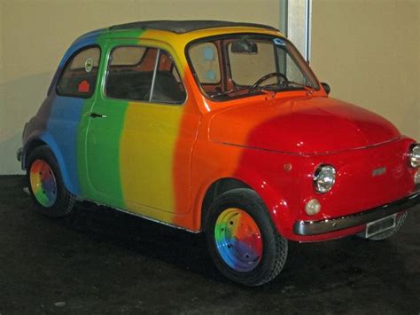 an old car painted in rainbow colors is parked next to a white wall and door