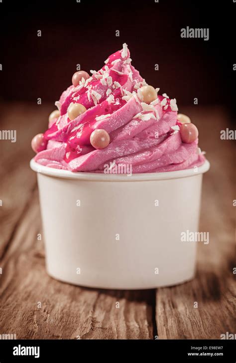 Party treat of decorated pink berry ice cream served in a plastic tub on a rustic wooden counter ...