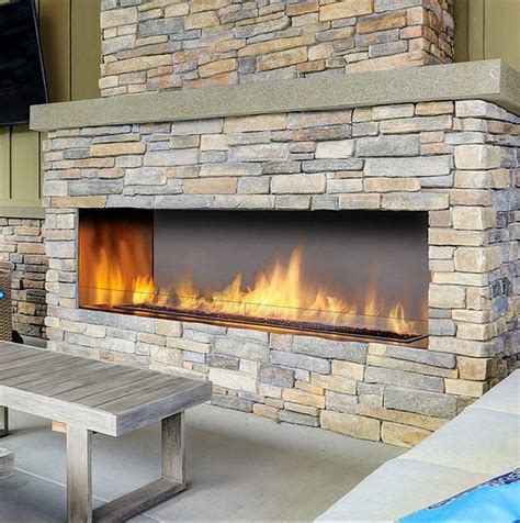 an outdoor fireplace with fire in it next to a picnic table and television on the wall