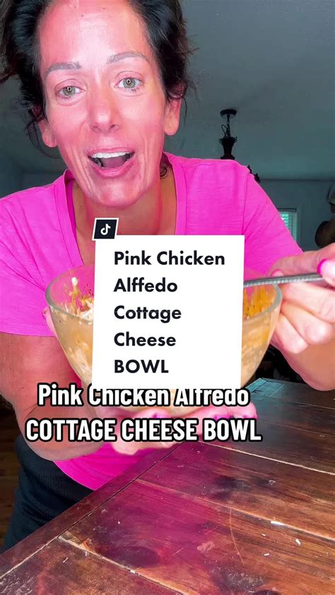 a woman in pink shirt holding up a sign with words on it that read pink chicken alfredo cheese bowl